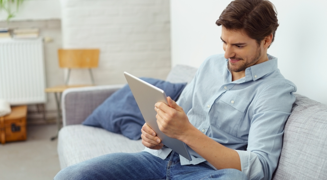 mann sitzt auf dem sofa und schaut auf sein tablet