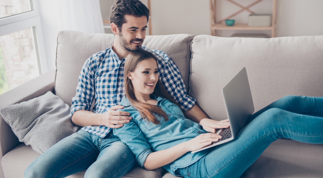So easy! Excited beautiful happy couple is doing online shopping in internet. They are indoors at home on cozy couch in casual clothes, relaxing and buying goods easily