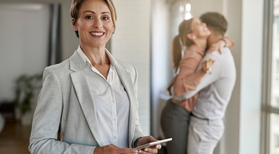 Portrait of happy real estate agent with joyful couple in the background.