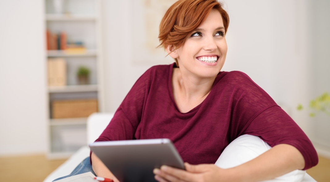 lachende junge frau sitzt auf dem sofa und hält tablet in der hand